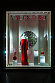 Rome, Italy, July 22 2017, A striking red dress is showcased in the shop window on Via Condotti, attracting evening pedestrians in Rome.