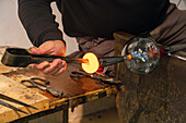 The glassblower creates an opening in the molten glass with jacks in a glassblowing demonstration in Venice, Italy.