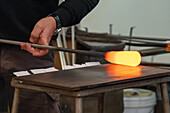 The glassblower rolls the molten gather on a marver in a glassblowing demonstration in Venice, Italy. Marvering creates a skin on the surface of the glass an begins to shape the gather.