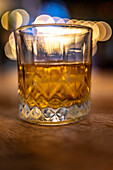 Close up of a whisky glass with a festive bokeh background, capturing the vibrant atmosphere of a wedding party in Malaga, Spain.