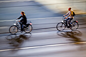 Dynamic panning photo capturing two cyclists riding through a city at night, creating a sense of speed and movement.