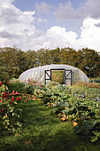Gewächshaus im Gemüsegarten mit üppigen Beeten im Vordergrund
