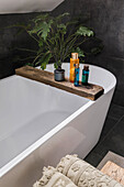 Freestanding bathtub with wooden shelf and care products in the modern bathroom