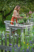 Woman sets table with herbs, vases with fennel, oregano, mint