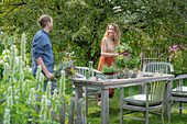 Couple in front of a laid table, vases with herbs, fennel, oregano, mint