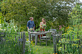Couple in front of a laid table, vases with herbs, fennel, oregano, mint