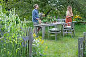 Couple in front of a laid table, vases with herbs, fennel, oregano, mint