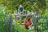 Couple with dog in front of a laid table, vases with herbs, fennel, oregano, mint