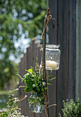 Mint, thyme, curry herb, oregano as a bouquet of herbs in a vase hanging on a branch with a tea light