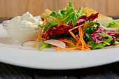 Salad with carrot strips, radishes and sour cream dip
