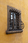 An ornate cast iron window grate on a building with Renaissance architecture in Florence, Italy.