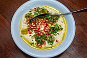 Pomegranate wirh Hummus dish. Closeup view. Arabic, vegetarian healthy food, snack or appetizer. Zajal restaurant Al Balad Steps, off Prince Muhammad Street, Al Rjoum, Amman, Jordan, Middle East. Umbrella street.