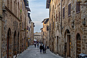 Tourists on the Via San Matteo in the medieval walled city of San Gimignano, Italy. At right is the Pesciolini Tower House.