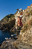 Small boats moored in the harbor in Riomaggiore, Cinque Terre, Italy with colorful buildings behind.