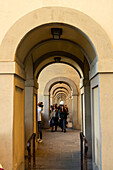 Touristen gehen durch die Kolonnade, die den Vasari-Korridor an der Ponte Vecchio in Florenz, Italien, stützt.