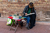 An artist paints watercolor scenes on the street in the medieval walled town of San Gimignano, Italy.