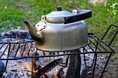 Kettle placed on a grill over a campfire, representing outdoor cooking in nature.