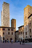 Tourists on the Piazza del Duomo with its towers in the medieval walled city of San Gimignano, Italy. L-R: Torri Salvucci, Torre Pettini and Torre Chigi.