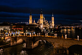 Aerial view of the Cathedral Basilica of Our Lady of the Pillar and Stone Bridge illuminated at night during Christmas, Zaragoza, Spain