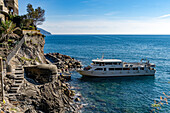 Ein Passagierfährschiff legt in Monterosso al Mare, Cinque Terre, Italien, an. Links ist ein Bunker aus dem Zweiten Weltkrieg zu sehen.