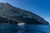 A high-speed commercial ferry boat anchored in the Bay of Naples off the shore of the island of Capri, Italy. The road to Anacapri is at top left with luxury resort hotels on top of the cliffs at center.