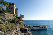 Eine Passagierfähre legt unterhalb des mittelalterlichen Aurora-Turms in Monterosso al Mare, Cinque Terre, Italien, an. Links ist ein Bunker aus dem Zweiten Weltkrieg zu sehen.