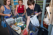 Poor and vulnerable families collecting donated products in the supermarket Rebost Solidari de Gracia, Gracia neighborhood, Barcelona, Spain, Europe. The Rebost Solidari de Gracia is a distributor entity of the Food Bank in its Sec, SERMA (fresh fruit and vegetables), cold chain (frozen and refrigerated products) and FEGA (products received from the EU) programs. An efficient management of all the food surpluses generated by the neighborhood (markets, supermarkets, shops, companies, restaurants, school canteens and others) is an important enough objective in itself, both for its use in the nei