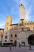 Tourists on the Piazza del Duomo with its towers in the medieval walled city of San Gimignano, Italy. L-R: Torre Chigi & Torre Rognosa.