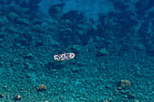 A tour boat with passengers in the crystal clear waters of the Tyrrhenian Sea by the island of Capri, Italy.