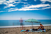 Peaceful beach scene with umbrella and vacationers enjoying sunshine and clear ocean view.