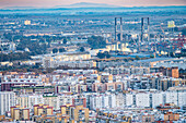 Urban landscape showcasing Los Remedios in Seville with the Centenario Bridge and the port in the backdrop during sunset.