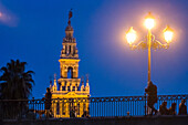 People walking on a bridge with Giralda Tower background in Seville during twilight.