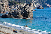 Tourists on the beach in off peak season at Monterosso al Mare, Cinque Terre, Italy. Behind is the Malpasso Rock.