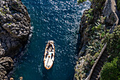 A small traditional fishing boat with tourists approaches the mouth of the Furore Fjord on the Amalfi Coast, Italy.