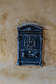 A weathered metal post box on the stuccoed wall going into the Cloisters of San Francesco in Sorrento, Italy.