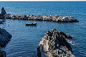 A small boat moored inside the breakwater of the harbor of the village of Manarola, Cinque Terre, Italy. Tourists take a selfie in the foreground.