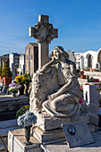 A cross and statue of a woman on a grave in a cemetery in Anacapri on the island of Capri, Italy.