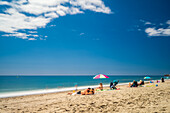 Peaceful beach scene with umbrella and vacationers enjoying sunshine and clear ocean view.