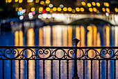 Intricate ironwork balustrade of Triana Bridge with colorful light reflections in a serene nighttime setting.