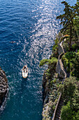 A small traditional fishing boat with tourists approaches the mouth of the Furore Fjord on the Amalfi Coast, Italy.