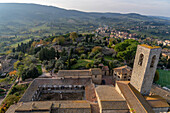 The campanile or bell tower of the Collegiata di Santa Maria Assunta in the medieval city of Gimignano, Italy. At left is the cloisters and behind are the ruins of a medieval fort and the Parco della Rocca.