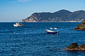 Fischerboote vor der zerklüfteten Küste der Cinque Terre in Manarola, Italien. In der Ferne liegt die Stadt Monterosso al Mare.