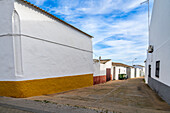 A narrow street lined with traditional whitewashed houses under a bright blue sky.