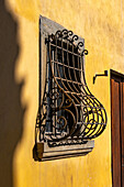 An ornate cast iron window grate on a building with Renaissance architecture in Florence, Italy.