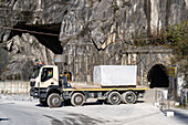 A truck hauling a huge marble block exits a tunnel in the marble quarries of Fantiscritti. Carrara, Italy.