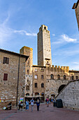 Tourists on the Piazza del Duomo with its towers in the medieval walled city of San Gimignano, Italy. L-R: Torre Chigi & Torre Rognosa.