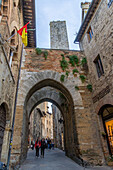 Tourists on Via San Matteo under the 13th Century Chancellery Gate in the medieval city of San Gimignano, Italy. Behind is one of the Salvucci Towers.