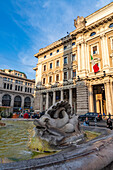 A carved dolphin in the Piazza Colonna fountain with the Galleria Albero Sordi shopping mall behind. Rome, Italy.