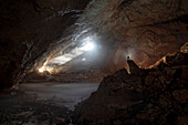 Wissenschaftler steht in Silhouette auf einer Felsformation in einer Eishöhle in den europäischen Alpen und betrachtet die natürliche Schönheit, die durch den Klimawandel gefährdet ist; Asiago, Venetien, Österreich