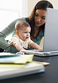 Mutter mit Laptop und Baby auf dem Schoß